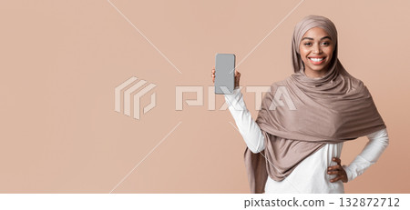 Happy afro muslim woman in hijab demonstrating modern smartphone with blank screen for mockup, posing over yellow background, free space Happy afro muslim woman in hijab demonstrating modern smartphone with blank screen for mockup, posing over yellow background, free space 132872712