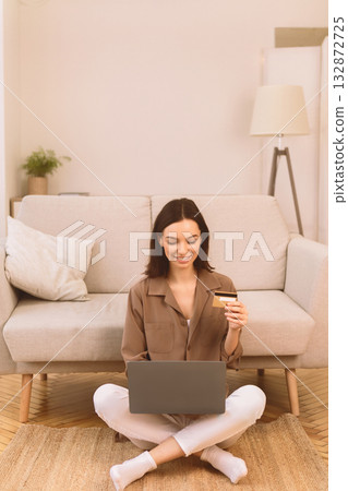 Online Store. Happy young woman doing shopping via internet using laptop and credit card, sitting on floor, copyspace 132872725
