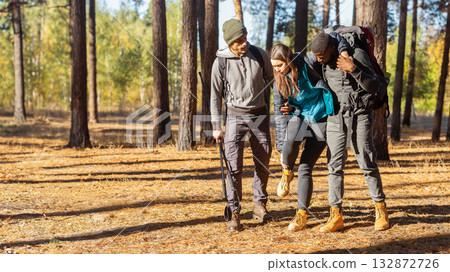 Multiracial guys supporting their female friend with injured anckle, hiking together at forest, free space Multiracial guys supporting their female friend with injured anckle, hiking together at forest, free space 132872726