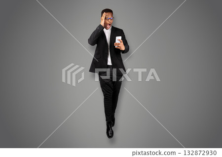 Always On Mobile. Full length of shocked black man using phone while jumping against white studio background Always On Mobile. Full length of shocked black man using phone while jumping against white studio background 132872930