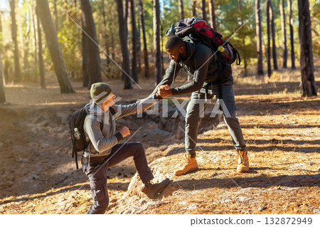 Two friends guys hiking together at countryside, black man helping caucasian guy to uphill, friendship concept 132872949