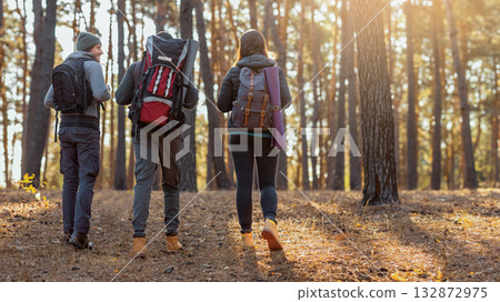 Three young friends with their backpacks on hiking trip in autumn forest, back view Three young friends with their backpacks on hiking trip in autumn forest, back view 132872975