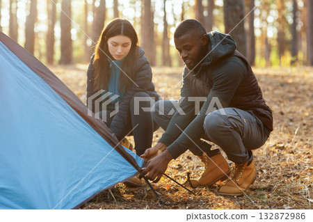 Young mixed race couple making tent together, having conversation, camping in forest Young mixed race couple making tent together, having conversation, camping in forest 132872986