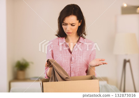 Puzzled Young Woman Taking Clothes Out Of Box, Holding Shirt, Getting Home Delivery By Mistake, Copyspace Puzzled Young Woman Taking Clothes Out Of Box, Holding Shirt, Getting Home Delivery By Mistake, Copyspace 132873016
