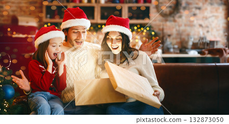 Christmas miracle. Surprised family of three looking into shining gift box, opening xmas presents together, kitchen interior Christmas miracle. Surprised family of three looking into shining gift box, opening xmas presents together, kitchen interior 132873050