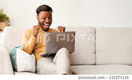 Yes. Excited Afro Man Using Laptop Computer Shaking Fists Celebrating Success Sitting On Sofa Indoor. Empty Space Yes. Excited Afro Man Using Laptop Computer Shaking Fists Celebrating Success Sitting On Sofa Indoor. Empty Space 132873126