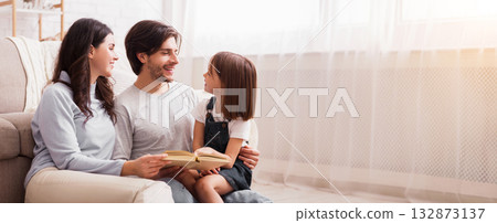 Early Development Concept. Little girl reading book with her parents, sitting on floor in living at home together, empty space 132873137