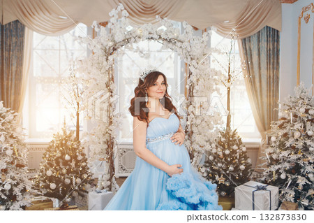 pregnant girl in a lush blue dress. girl with dark hair wearing a crown. christmas decoration. High quality photo 132873830
