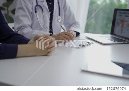 Doctor and a patient are sitting at the white table in clinic. The female physician is using clipboard for making notes during a consultation, close up. Medicine concept Doctor and a patient are sitting at the white table in clinic. The female physician is using clipboard for making notes during a consultation, close up. Medicine concept 132876974