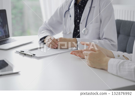 Doctor and a patient. The female physician is listening carefully and making notes during a consultation in the clinic, close up. Medicine 132876992