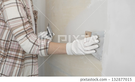 Unknown female construction worker wearing protective gloves applying plaster, smoothing wall surface during home renovation work Unknown female construction worker wearing protective gloves applying plaster, smoothing wall surface during home renovation work 132877015