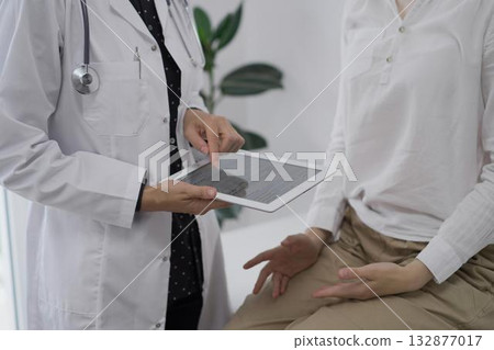 Doctor and a patient. The female physician is using a tablet computer besides a young woman during a consultation in the clinic, view above. Medicine concept 132877017