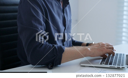Professional businessman typing on laptop, surrounded by financial reports and digital tablet, working in contemporary corporate workspace. Business people concept 132877021