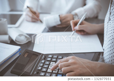 Two accountants use a calculator and laptop computer for counting taxes or revenue balance. Business, audit, and taxes concepts Two accountants use a calculator and laptop computer for counting taxes or revenue balance. Business, audit, and taxes concepts 132877031