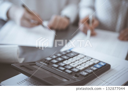 Calculator is waiting to be used while Two accountants are ready to count taxes or make a revenue balance in the background. Business, audit, and taxes concepts Calculator is waiting to be used while Two accountants are ready to count taxes or make a revenue balance in the background. Business, audit, and taxes concepts 132877044