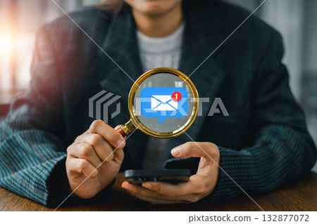 Business professional using a smartphone and magnifying glass to analyze email marketing strategies for effective communication. 132877072