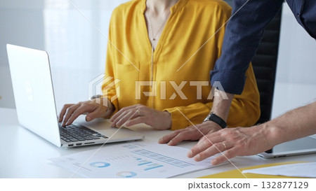 Business colleagues collaborating on a project while analyzing financial charts and entering data on a laptop in a modern office. Businesspeople concept 132877129
