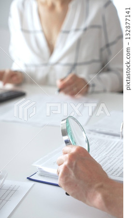 Groupe of professional accountants working together, using a magnifying glass and a calculators, to audit financial reports in their brightly lit office. Audit and taxes concept 132877141
