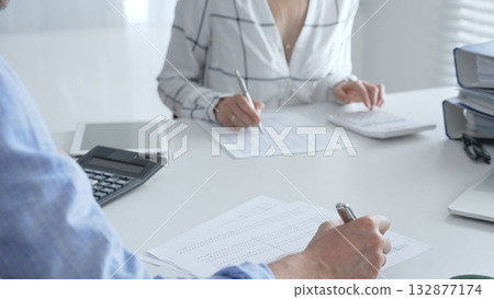Accounting team working together, reviewing financial reports, using calculator, analyzing data while working at sleek corporate workspace. Audit and taxes concept 132877174