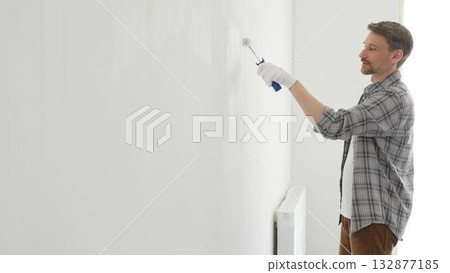Professional house painter applying white paint to an interior wall with a roller during home renovation. Focus on the skilled hand maneuvering the tool for a fresh, clean finish Professional house painter applying white paint to an interior wall with a roller during home renovation. Focus on the skilled hand maneuvering the tool for a fresh, clean finish 132877185