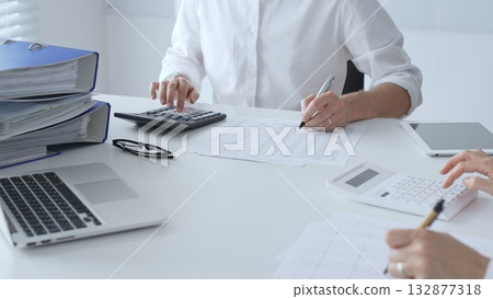 Two accountants collaborating in a well lit office, analyzing financial data and preparing reports with calculators and pens. Audit and taxes in business Two accountants collaborating in a well lit office, analyzing financial data and preparing reports with calculators and pens. Audit and taxes in business 132877318
