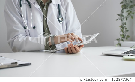 Doctor woman in lab coat and stethoscope using digital tablet at desk in medical office, accessing online patient information. Medicine and health care concept Doctor woman in lab coat and stethoscope using digital tablet at desk in medical office, accessing online patient information. Medicine and health care concept 132877364