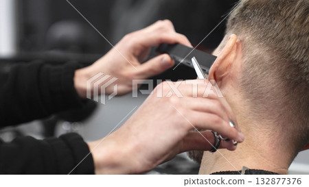 Professional barber grooming client's beard with precision, using comb and razor within stylish contemporary barbershop setting 132877376