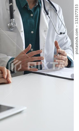 Doctor man wearing medical coat over green shirt, and stethoscope is gesturing with hands over white table and medical records while explaining diagnosis to patient. Medicine and health care concept 132877553