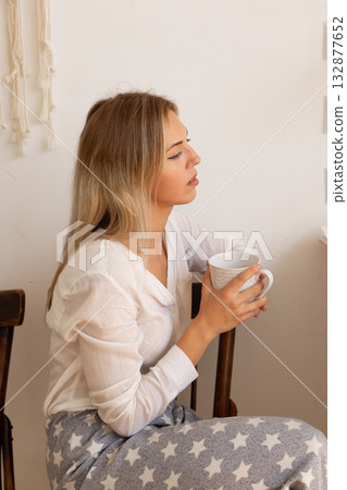 Woman holding mug and looking aside while sitting at home in peaceful atmosphere. Reflection, rest and mindfulness in modern life. 132877652