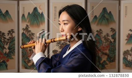 Asian woman in traditional blue hanbok playing bamboo flute danso against Korean landscape painting folding screen background 132878830