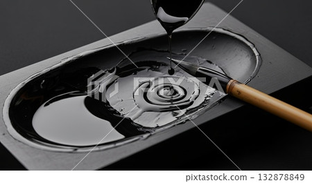 Traditional Chinese calligraphy artist painting black ink with bamboo brush on ceramic inkstone palette creating spiral swirl pattern 132878849