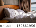 Unmade bed with white pillows and duvet in sunny hotel room with sea view 132881956