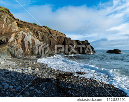 Serene ocean view. The pebble beach is touched by the waves under a cloudy sky. Serene ocean view. The pebble beach is touched by the waves under a cloudy sky. 132882291