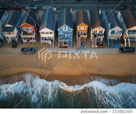 Colorful beachfront houses lined along sandy shore at sunset with waves lapping beach and coastal road behind 132882585