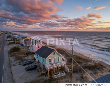 Coastal pastel beach houses on stilts at sunset with dramatic clouds and rolling waves creating tranquil seaside mood Coastal pastel beach houses on stilts at sunset with dramatic clouds and rolling waves creating tranquil seaside mood 132882588