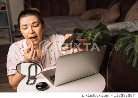 Woman fixing lips while holding phone by laptop 132882897