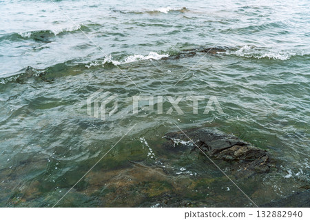 Clear lake waves rippling over dark shoreline rocks 132882940