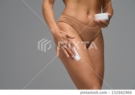 Woman applying moisturizing cream on thigh as part of body care and skincare Woman applying moisturizing cream on thigh as part of body care and skincare 132882960