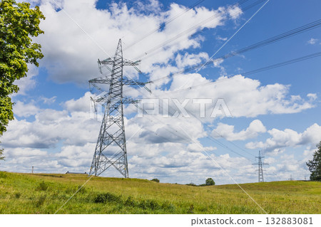 High voltage power lines and steel transmission towers across rural meadow 132883081