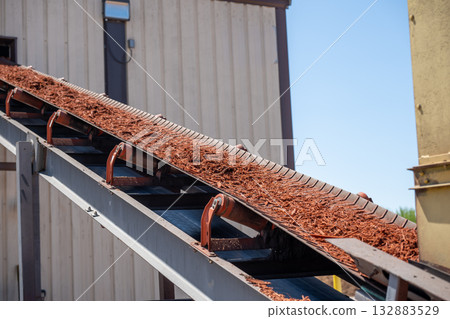 Conveyor belt transporting mulch at a landscaping supply facility on a sunny day 132883529