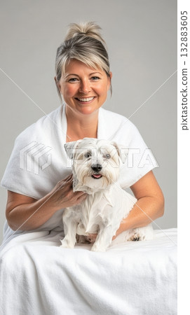 Middle-Aged Woman Blow-Drying Freshly Bathed West Highland White Terrier with Soft Towel in Clean Studio Setting 132883605