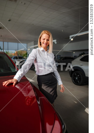 Smiling woman examining red car in car dealership showroom 132883859