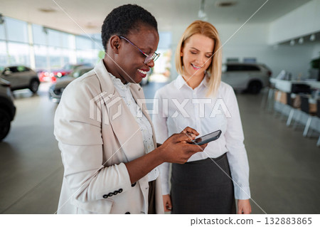Car salesperson showing car features on smartphone to customer 132883865