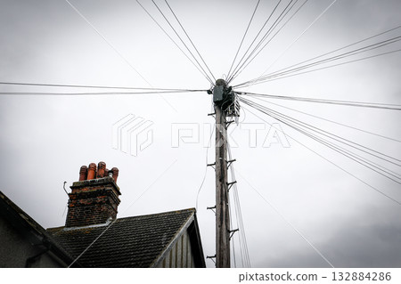 Wooden utility pole with multiple overhead wires near house chimney under cloudy sky Wooden utility pole with multiple overhead wires near house chimney under cloudy sky 132884286