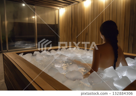 Woman relaxing in wooden ice bath spa tub, practicing cold plunge therapy for wellness and balance. 132884306