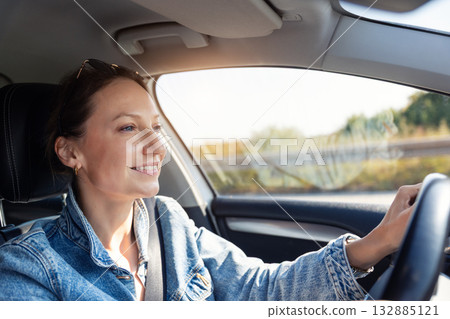 Portrait young adult happy smiling woman in sunglasses drives sunny highway road wearing denim jacket. Light reflects face enjoys relaxed travel trip moment countryside bright spring summer weather Portrait young adult happy smiling woman in sunglasses drives sunny highway road wearing denim jacket. Light reflects face enjoys relaxed travel trip moment countryside bright spring summer weather 132885121