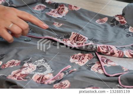 A woman is reviewing pajamas. She is examining the shirt. The pajamas consist of pants and a button-up shirt. Close-up. 132885139