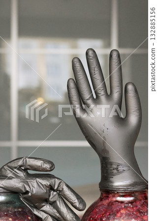 Two glass jars with fermenting grapes. Black rubber gloves are put on the jars. One glove is inflated by fermentation gases. Making homemade grape wine. Close-up 132885156