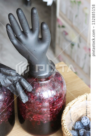 Two glass jars with fermenting grapes. Black rubber gloves are put on the jars. One glove is inflated by fermentation gases. Making homemade grape wine. Two glass jars with fermenting grapes. Black rubber gloves are put on the jars. One glove is inflated by fermentation gases. Making homemade grape wine. 132885158