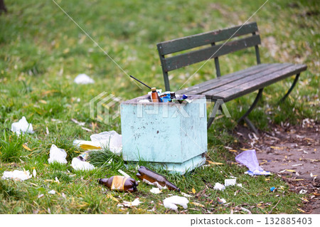 A trash can is positioned right next to a bench that is located in a park A trash can is positioned right next to a bench that is located in a park 132885403